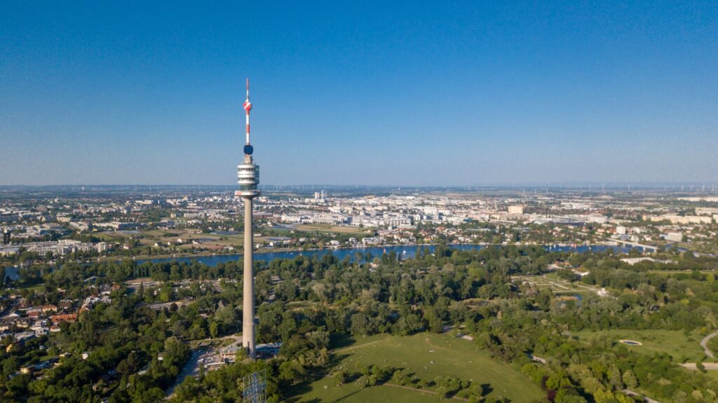 Der Wiener Donauturm aus der Luftperspektive, ein schlanker Aussichtsturm mit Panoramablick, umgeben von grünen Parkanlagen und der Donau.