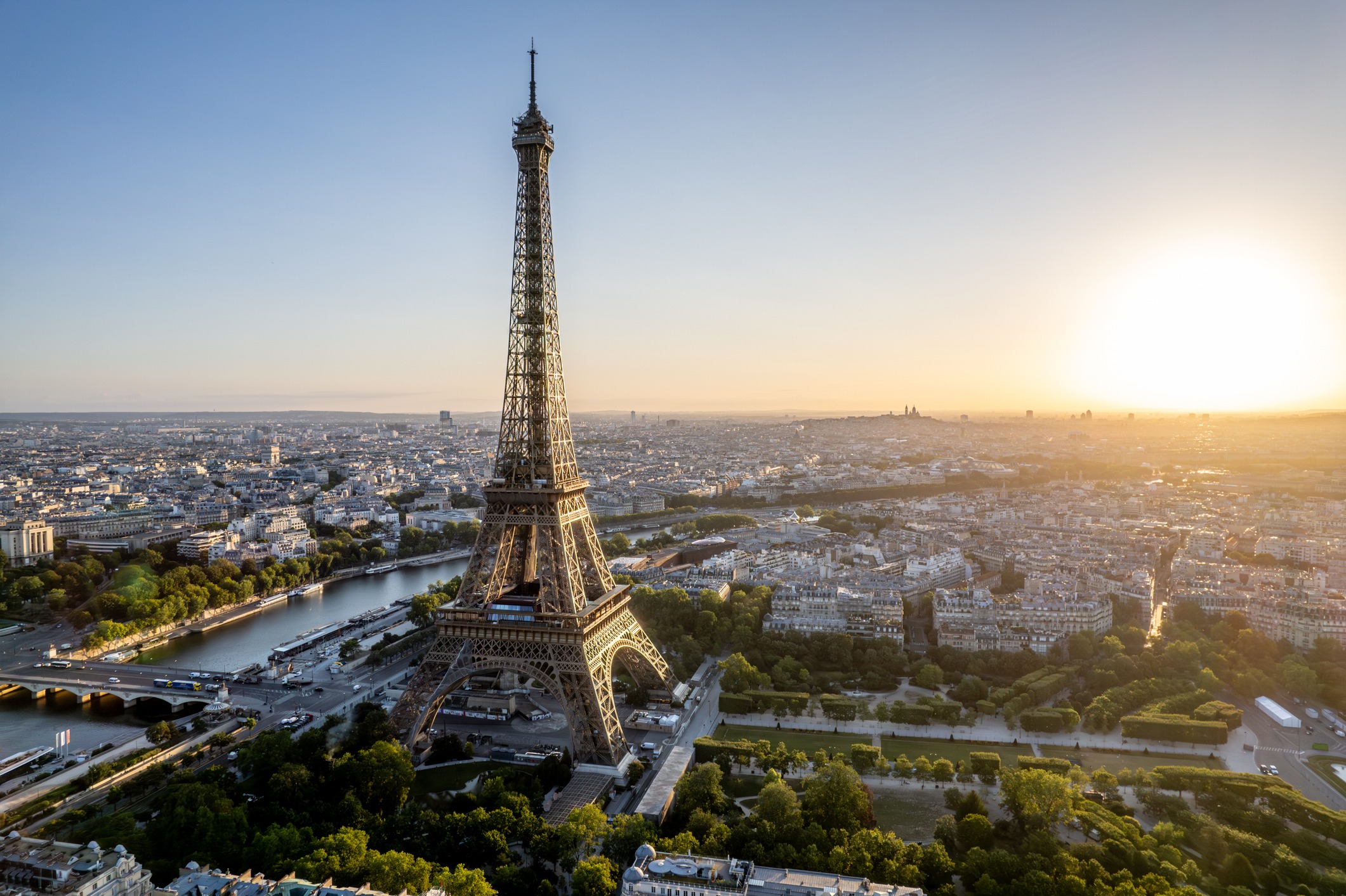 Luftaufnahme von Paris mit dem Eiffelturm im Zentrum, umgeben von historischen Gebäuden, der Seine und grünen Stadtflächen.