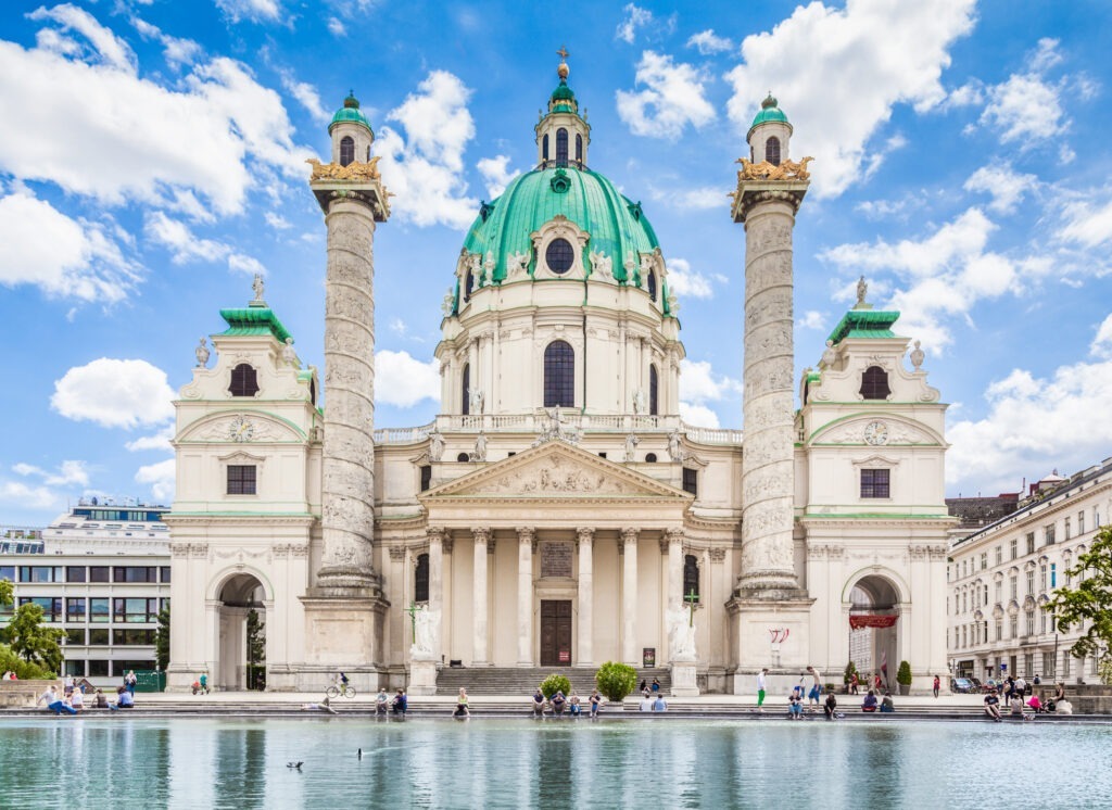 Die Wiener Karlskirche am Karlsplatz, ein prachtvolles barockes Gotteshaus mit markanter Kuppel und reflektierendem Wasserbecken im Vordergrund.