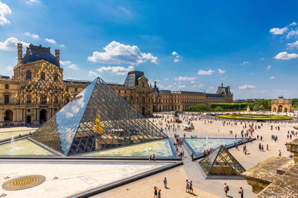 Blick auf das Louvre-Museum in Paris mit der ikonischen Glaspyramide im Vordergrund, umgeben von beeindruckender historischer Architektur.