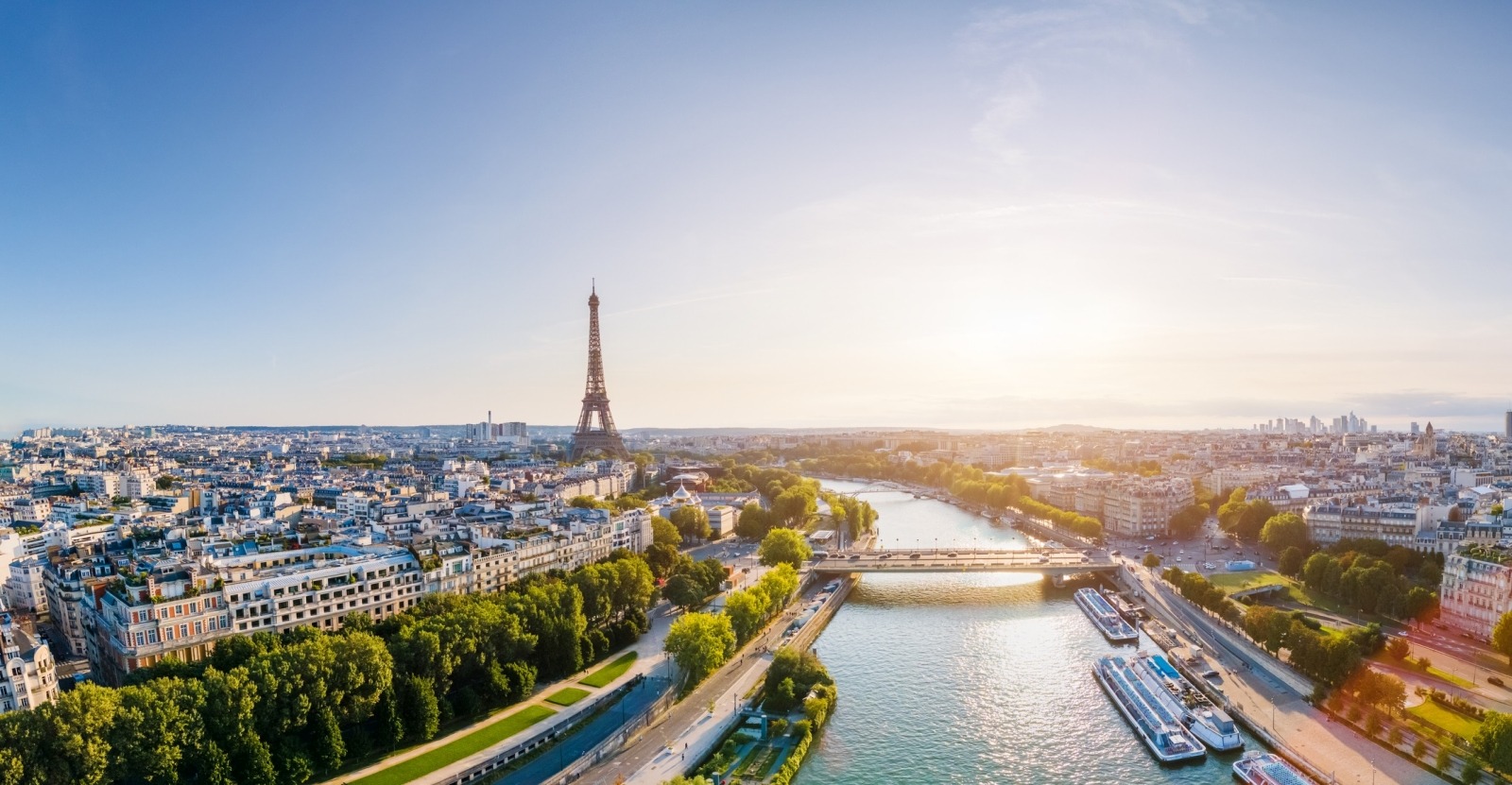 Luftaufnahme von Paris mit der Seine, dem Eiffelturm und umliegenden historischen Gebäuden an einem sonnigen Tag, die den Charme der Stadt einfangen.