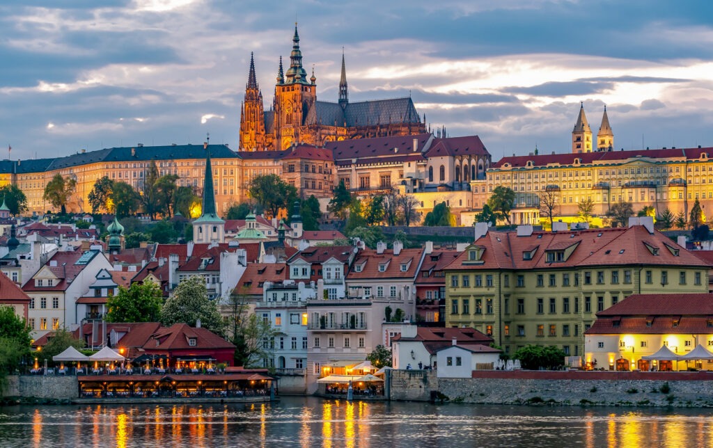 Panorama der Prager Burg mit der St.-Veits-Kathedrale im warmen Licht des Sonnenuntergangs, umgeben von den historischen Gebäuden der Kleinseite in Prag, Tschechien.