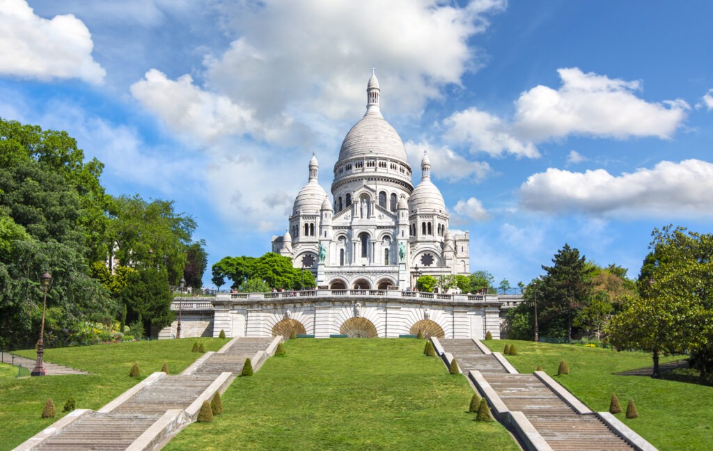 Die Basilika Sacré-Cœur auf dem Montmartre-Hügel in Paris, ein strahlend weißes Wahrzeichen mit markanter Kuppel, umgeben von grünen Parkanlagen.