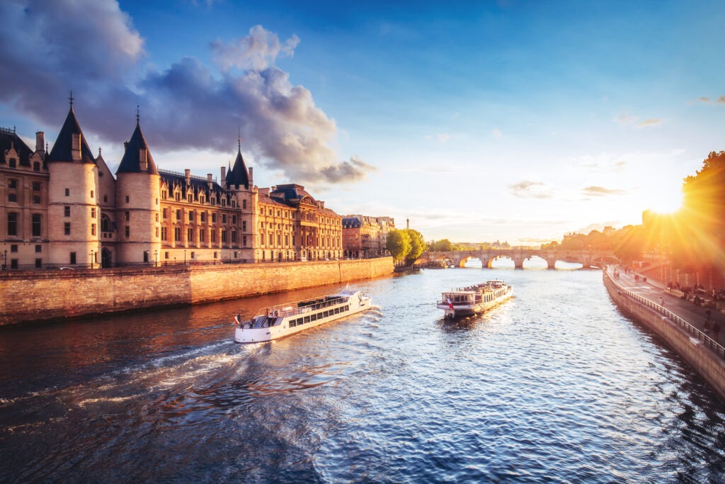 Dramatischer Sonnenuntergang über den Seine-Ufern mit der historischen Conciergerie und reflektierenden Farben im Wasser.