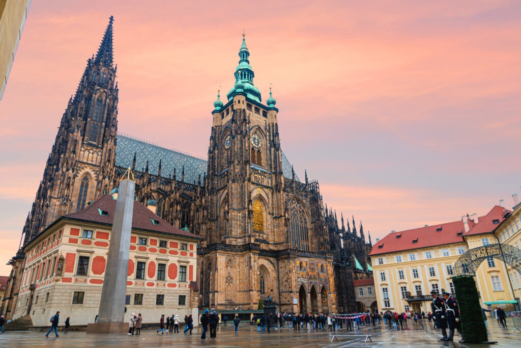 Der St.-Veits-Dom auf der Prager Burg in Prag, Tschechien, unter einem dramatischen Himmel bei Sonnenuntergang, mit leuchtenden Farben, die die gotische Architektur hervorheben.