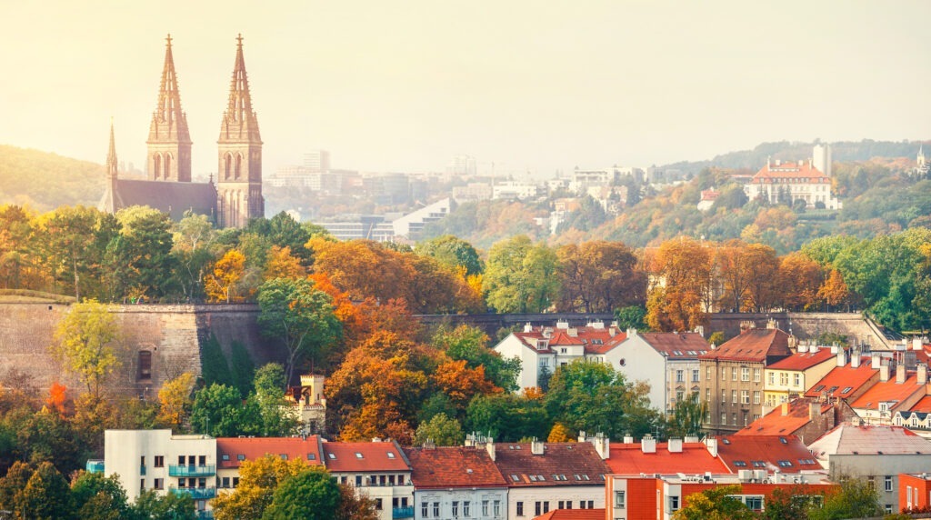 Blick auf Prag bei Sonnenuntergang mit der historischen Festung Vyšehrad, umgeben von roten Ziegeldächern und der malerischen Stadtlandschaft entlang der Moldau.