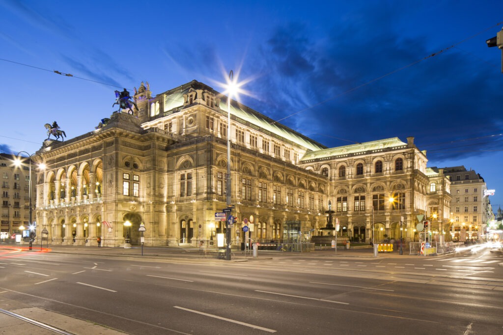 Die Wiener Staatsoper, ein prächtiges historisches Opernhaus mit eindrucksvoller Architektur und festlicher Beleuchtung in der Abenddämmerung.