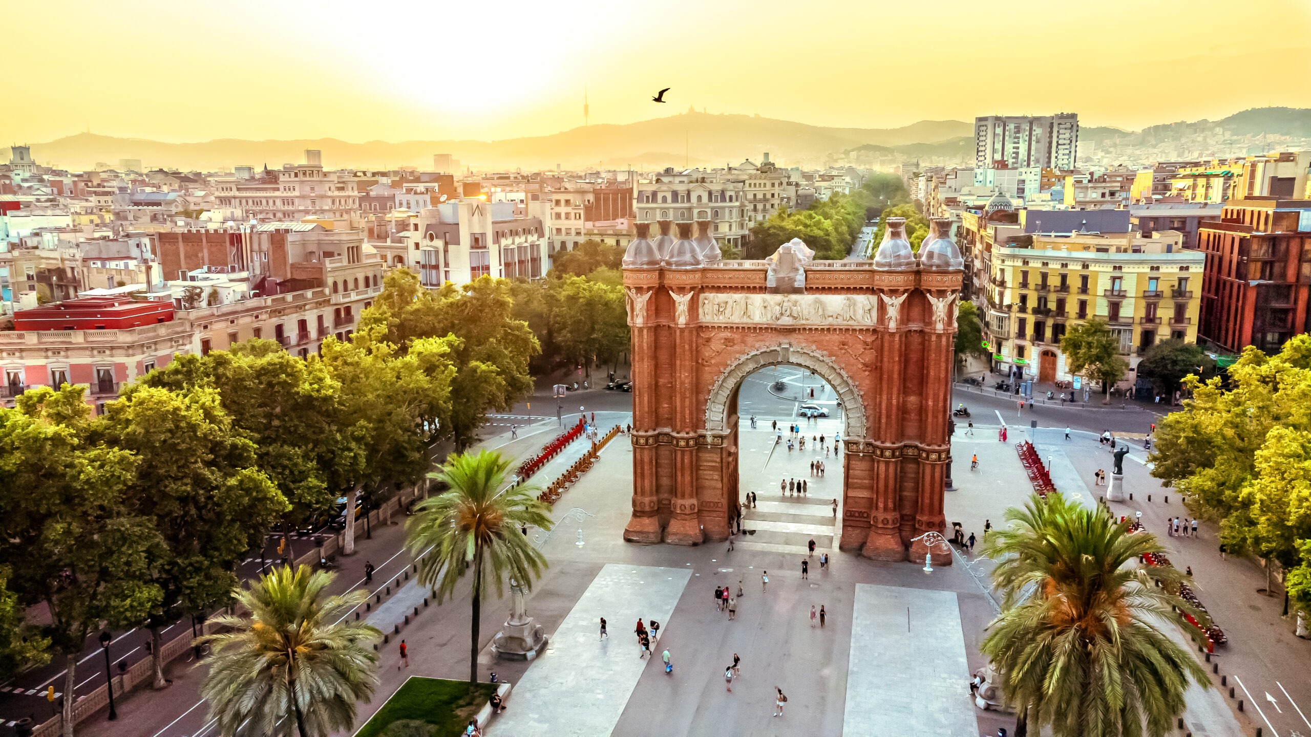 Luftaufnahme des Arc de Triomf in Barcelona, Spanien, umgeben von Palmen, Fußgängern und lebendiger Stadtatmosphäre.