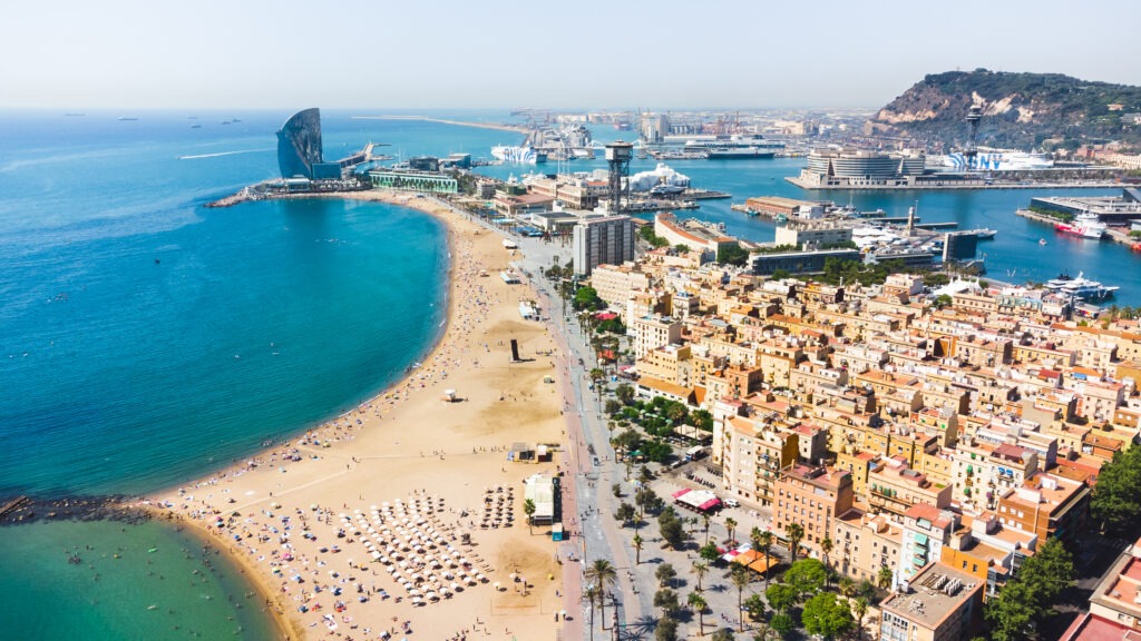 Luftaufnahme des Strandes La Barceloneta in Barcelona, mit goldenem Sand, blauem Meer und lebhafter Strandpromenade.