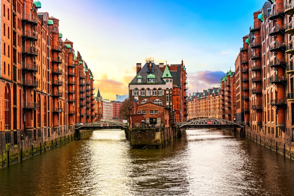 Die historische Speicherstadt in Hamburg bei Sonnenuntergang, mit beleuchteten Backstein-Lagerhäusern und Spiegelungen im Wasser.