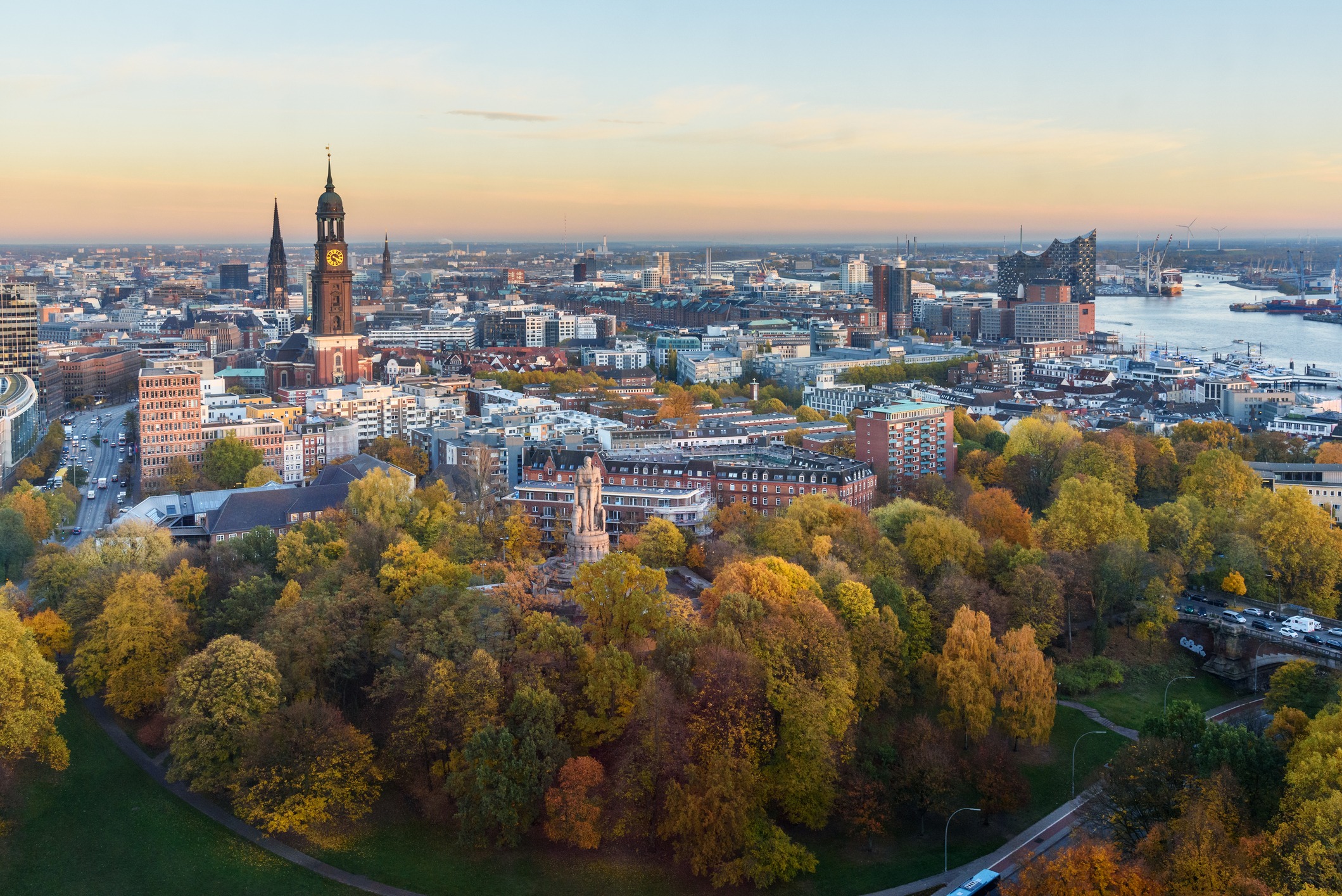 Blick auf Hamburg bei Sonnenuntergang mit Michel, Hafen und Elbphilharmonie im Hintergrund.