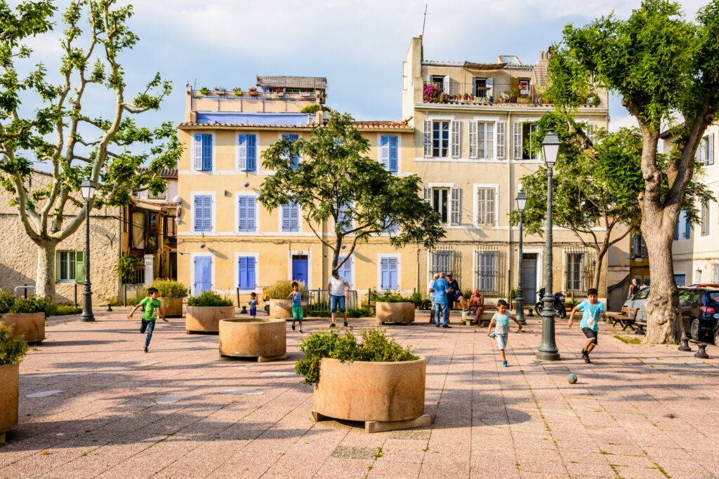 Kinder spielen Fußball auf dem Place des Moulins im historischen Viertel Le Panier in Marseille, umgeben von malerischen Altstadtgebäuden.