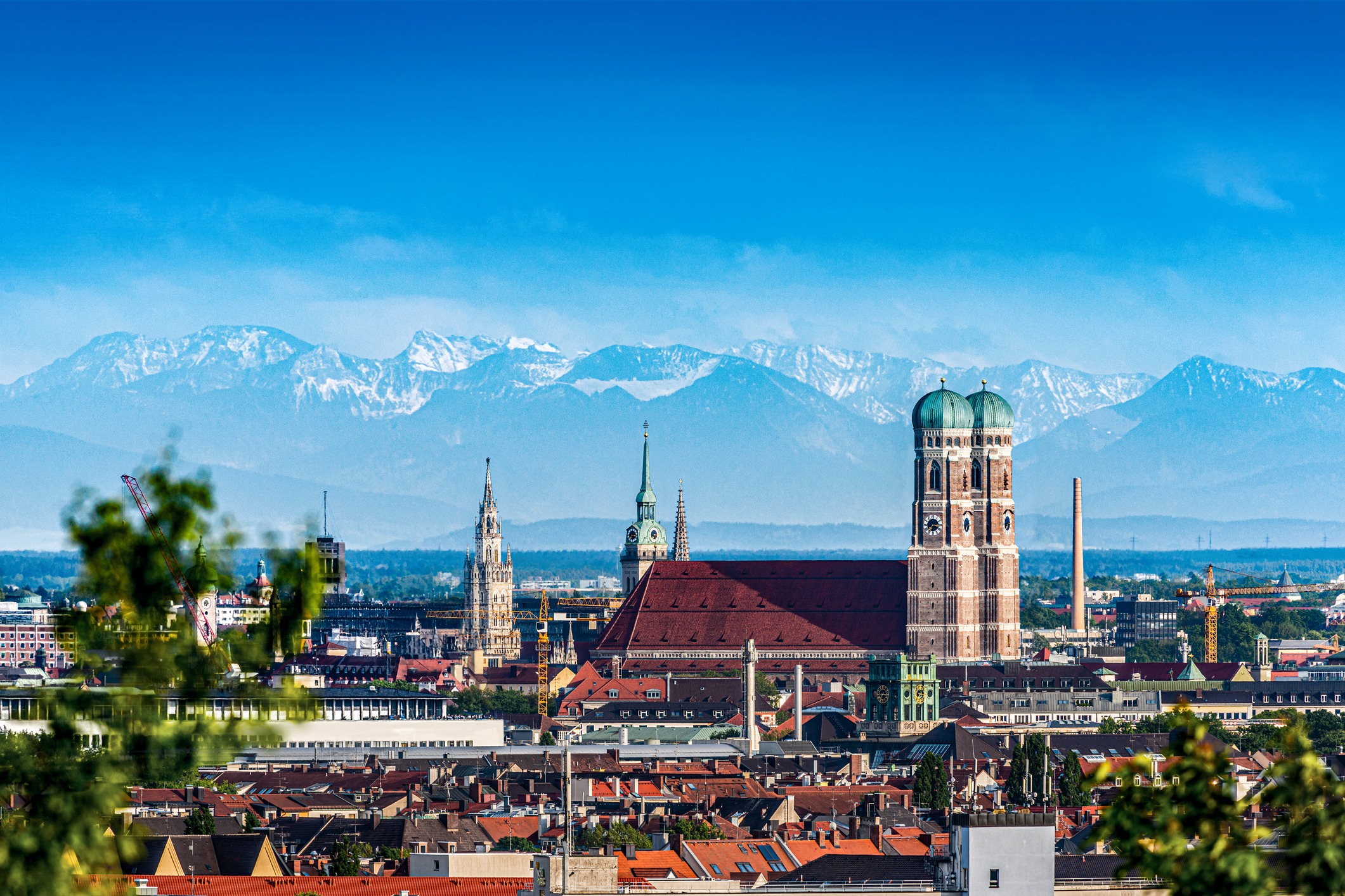 Panoramablick auf München mit Frauenkirche und Alpen im Hintergrund.