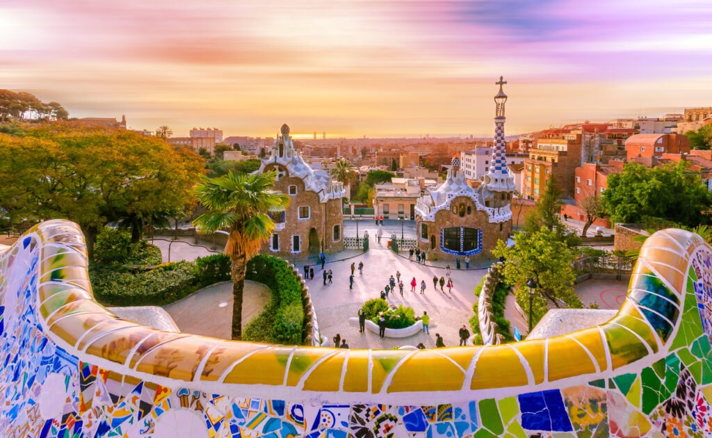 Panoramablick auf Barcelona vom Park Güell, mit farbenfrohen Mosaiken und der Skyline der Stadt im Hintergrund.