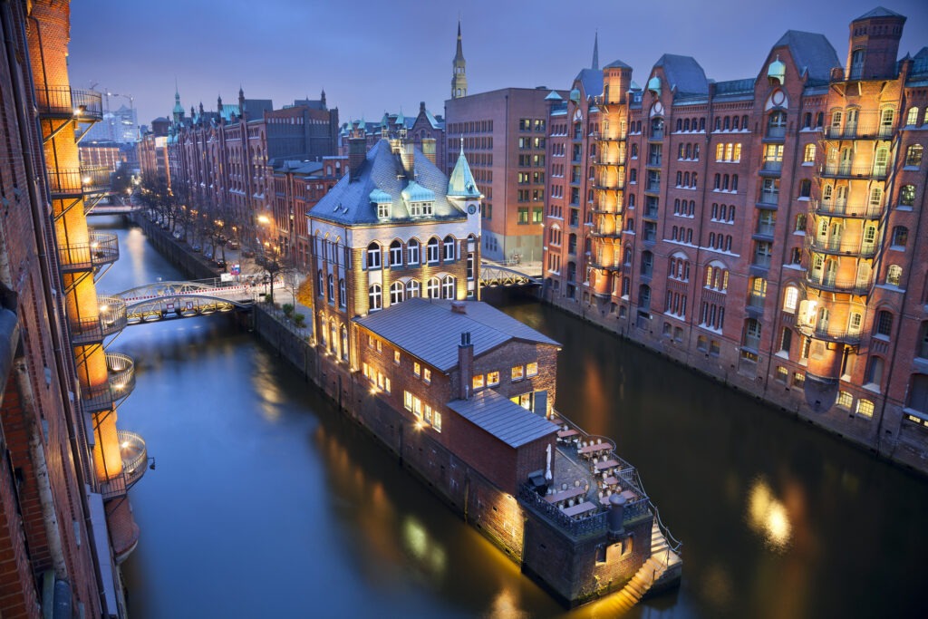 Hamburgs Speicherstadt bei Abenddämmerung, mit beleuchteten Backsteingebäuden und reflektierenden Kanälen.