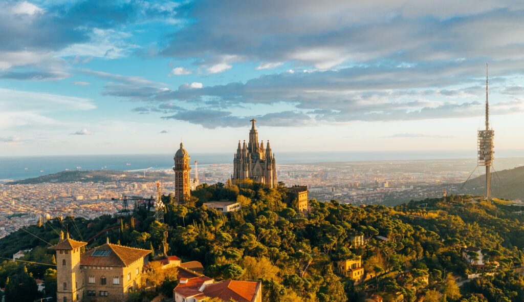 Luftaufnahme der Skyline von Barcelona mit dem Tibidabo und der beleuchteten Sagrat Cor Kirche im Hintergrund.